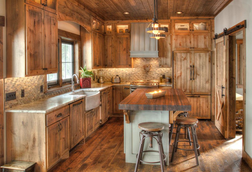 Mid-sized country l-shaped eat-in kitchen in Minneapolis with a farmhouse sink, recessed-panel cabinets, medium wood cabinets, granite benchtops, multi-coloured splashback, slate splashback, panelled appliances, dark hardwood floors, with island and beige benchtop.