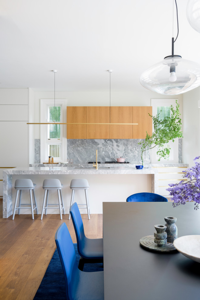 This is an example of a large contemporary eat-in kitchen in Sydney with an undermount sink, flat-panel cabinets, limestone benchtops, grey splashback, medium hardwood floors, with island and grey benchtop.