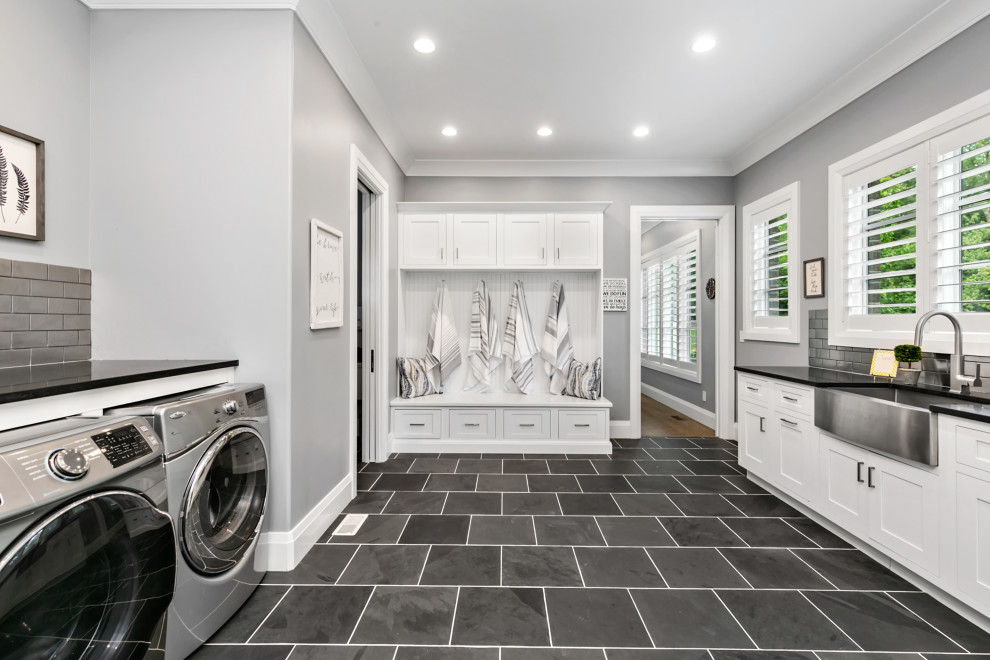 Traditional l-shaped utility room in St Louis with a farmhouse sink, shaker cabinets, white cabinets, grey splashback, subway tile splashback, grey walls, a side-by-side washer and dryer, grey floor and black benchtop.