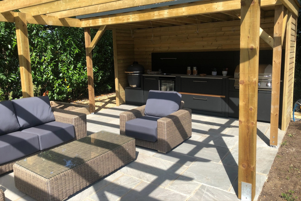 Small contemporary backyard patio in Hampshire with an outdoor kitchen, natural stone pavers and a pergola.