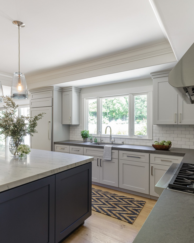 This is an example of a large transitional l-shaped open plan kitchen in San Francisco with a single-bowl sink, shaker cabinets, white cabinets, grey splashback, panelled appliances, light hardwood floors, with island, brown floor and marble benchtops.