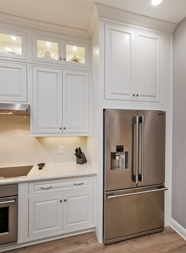 This is an example of a mid-sized transitional galley open plan kitchen in Jacksonville with an undermount sink, beaded inset cabinets, white cabinets, quartz benchtops, white splashback, ceramic splashback, stainless steel appliances, vinyl floors, a peninsula, beige floor and grey benchtop.