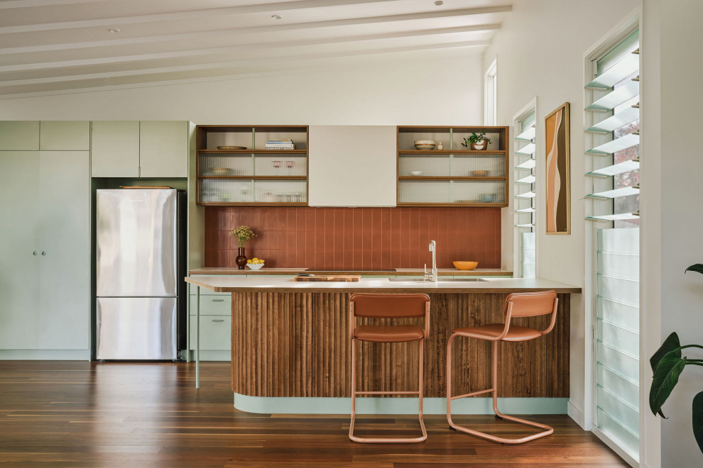 Photo of a midcentury galley kitchen in Gold Coast - Tweed with an undermount sink, flat-panel cabinets, green cabinets, red splashback, stainless steel appliances, dark hardwood floors, with island, brown floor, white benchtop and vaulted.