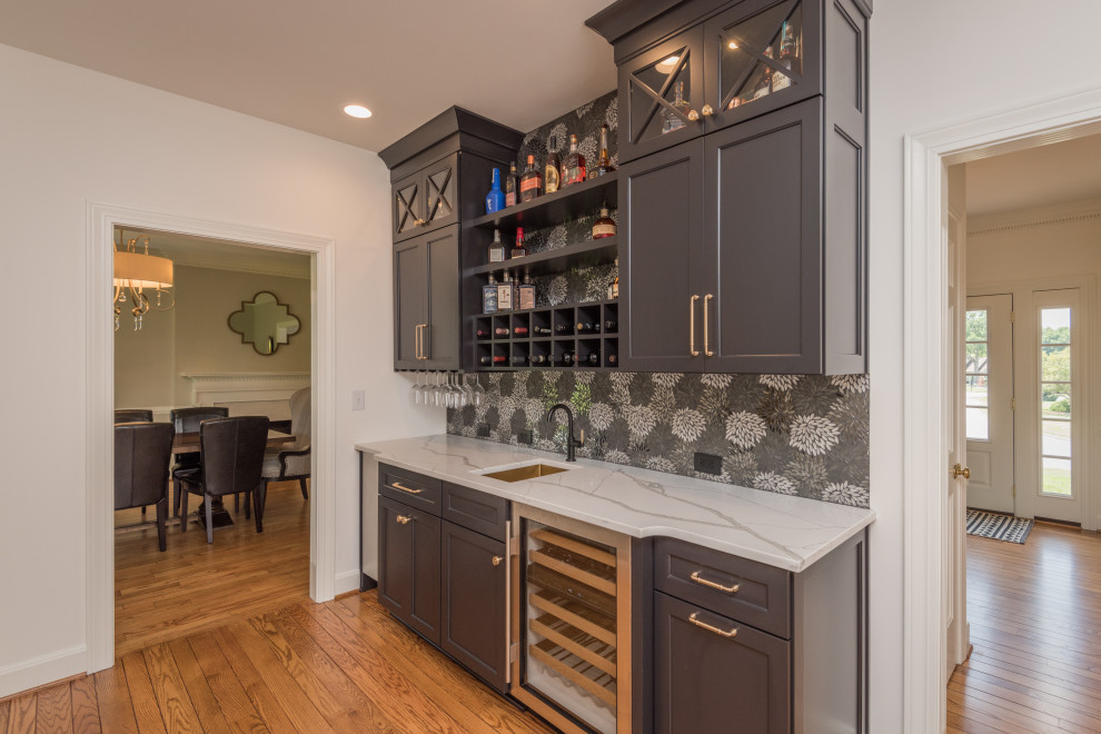 Photo of a transitional single-wall wet bar in Louisville with an undermount sink, shaker cabinets, grey cabinets, grey splashback, medium hardwood floors, brown floor and white benchtop.