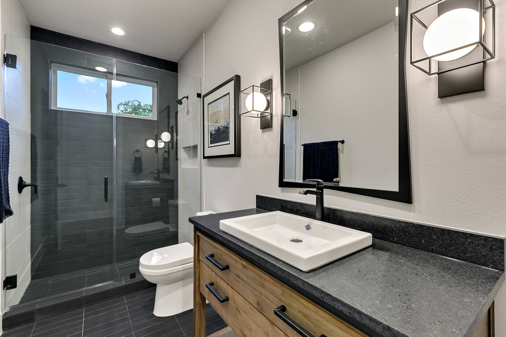 Photo of a contemporary bathroom in Austin with distressed cabinets, an alcove shower, gray tile, porcelain tile, grey walls, porcelain floors, a vessel sink, granite benchtops, beige floor, a hinged shower door, black benchtops, a single vanity and a freestanding vanity.