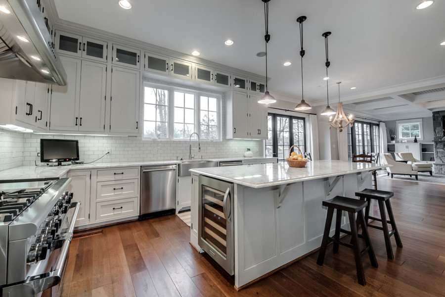 Large arts and crafts u-shaped eat-in kitchen in DC Metro with a farmhouse sink, shaker cabinets, white cabinets, granite benchtops, white splashback, subway tile splashback, stainless steel appliances, medium hardwood floors and with island.