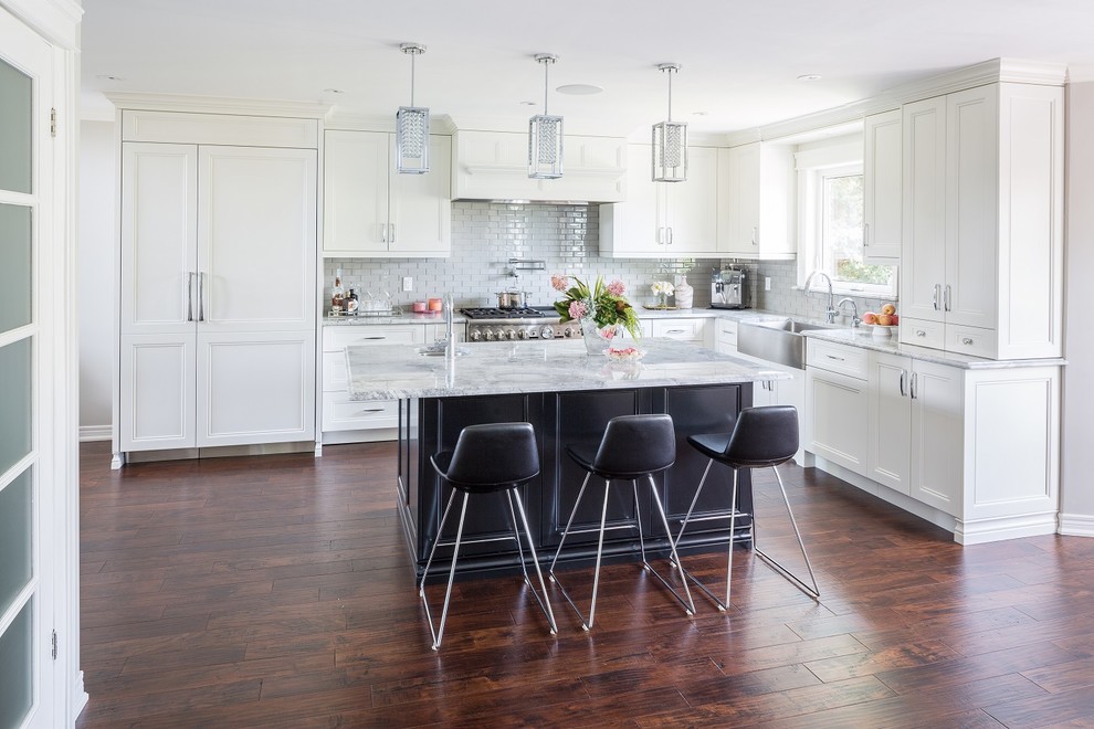 Example of a large transitional l-shaped dark wood floor and brown floor kitchen design in Toronto with a farmhouse sink, shaker cabinets, gray backsplash, ceramic backsplash, stainless steel appliances, an island and white countertops