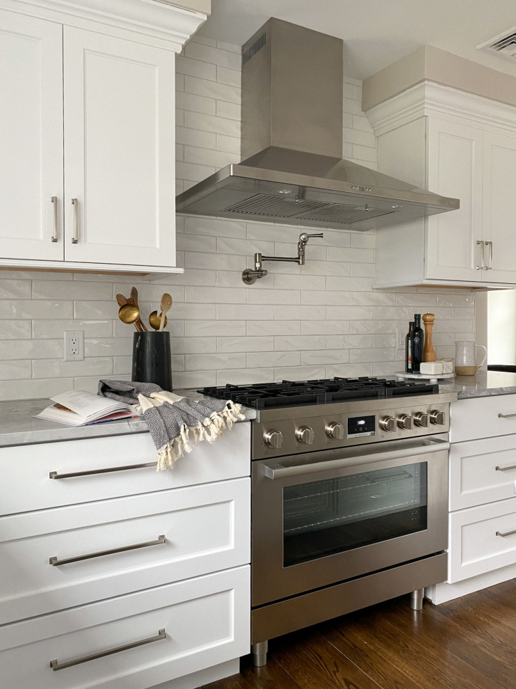 This is an example of a traditional kitchen in Boston with a submerged sink, shaker cabinets, white cabinets, quartz worktops, white splashback, ceramic splashback, stainless steel appliances, medium hardwood flooring and an island.
