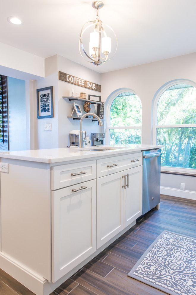 Photo of a mid-sized transitional u-shaped separate kitchen in Orlando with an undermount sink, shaker cabinets, white cabinets, quartz benchtops, white splashback, marble splashback, stainless steel appliances, porcelain floors, with island and brown floor.