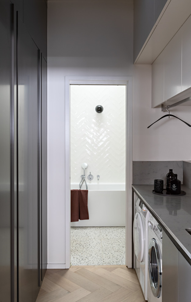 This is an example of a contemporary l-shaped laundry room in Melbourne with an undermount sink, flat-panel cabinets, white cabinets, light hardwood floors, beige floor and white benchtop.