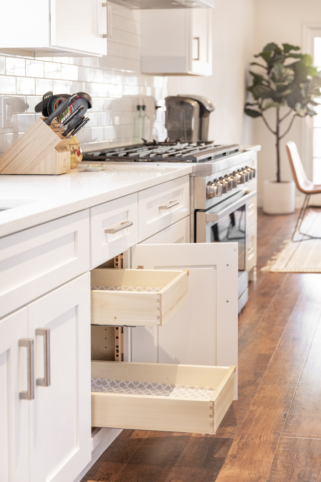 Mid-sized transitional medium tone wood floor and brown floor eat-in kitchen photo in Phoenix with shaker cabinets, white cabinets, white backsplash, subway tile backsplash, stainless steel appliances and an island