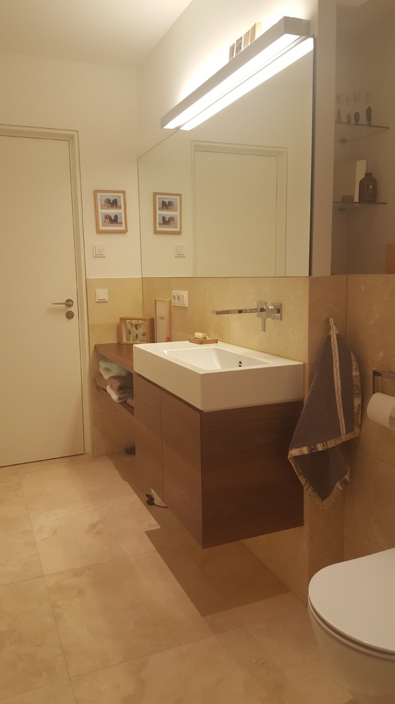 Duschbad With flächenbündigen Schrankfronten, dunklen Holzschränken, Duschnische, Wandtoilette, beigen Fliesen, Travertinfliesen, beiger Wandfarbe, Travertin, Wandwaschbecken, Edelstahl-Waschbecken/Waschtisch, beigem Boden and Schiebetür-Duschabtrennung in Berlin