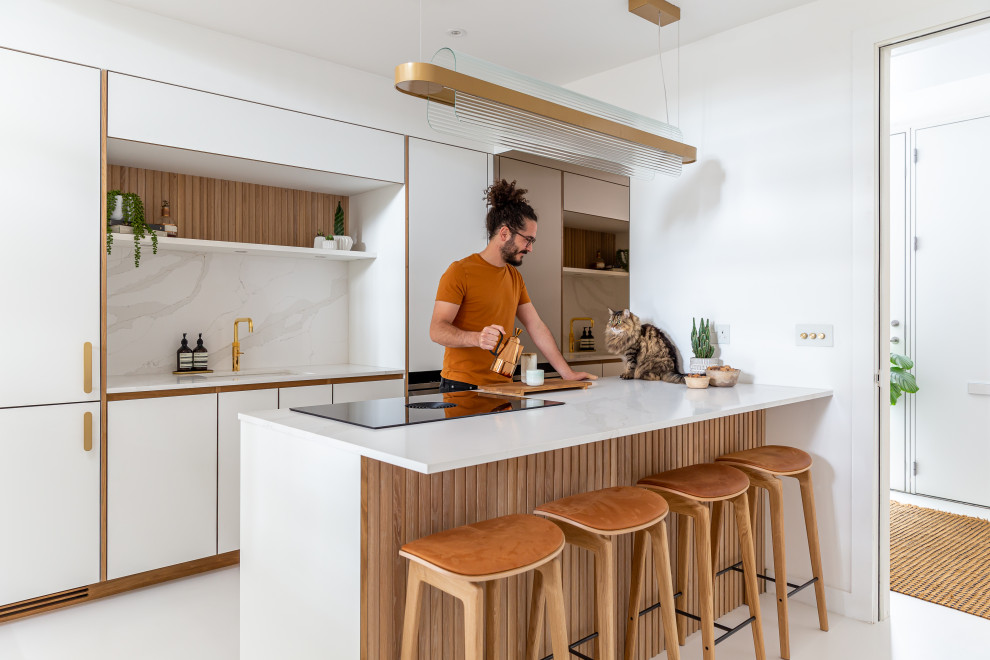 This is an example of a scandinavian kitchen in London with flat-panel cabinets, white cabinets, solid surface benchtops, white splashback, white benchtop, an undermount sink, panelled appliances, a peninsula and white floor.