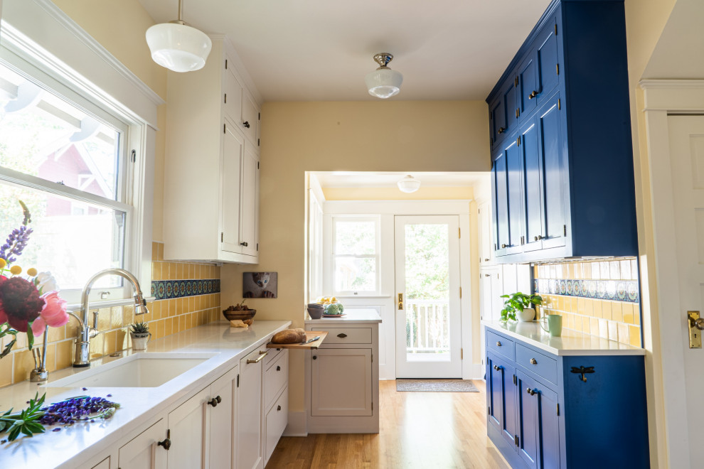Idéer för att renovera ett vit vitt l-kök, med en undermonterad diskho, skåp i shakerstil, blå skåp, bänkskiva i kvarts, gult stänkskydd, stänkskydd i keramik, integrerade vitvaror, mellanmörkt trägolv och brunt golv