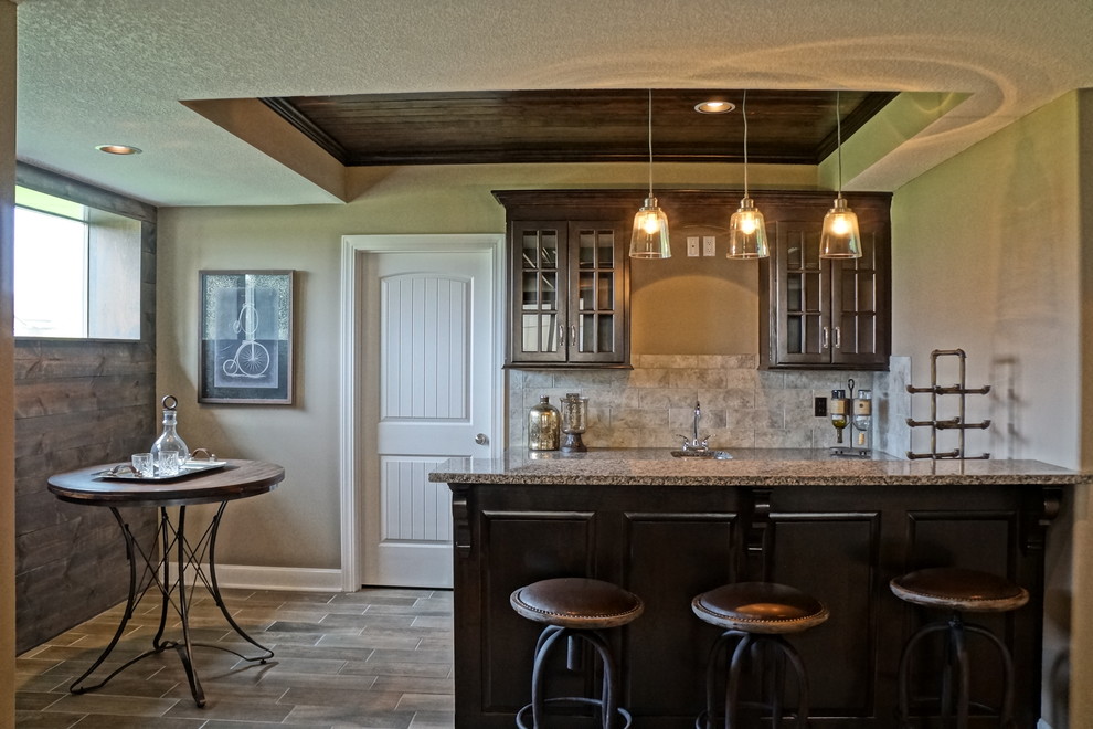 Design ideas for a mid-sized traditional l-shaped seated home bar in Kansas City with an undermount sink, glass-front cabinets, dark wood cabinets, granite benchtops, grey splashback, porcelain splashback and porcelain floors.