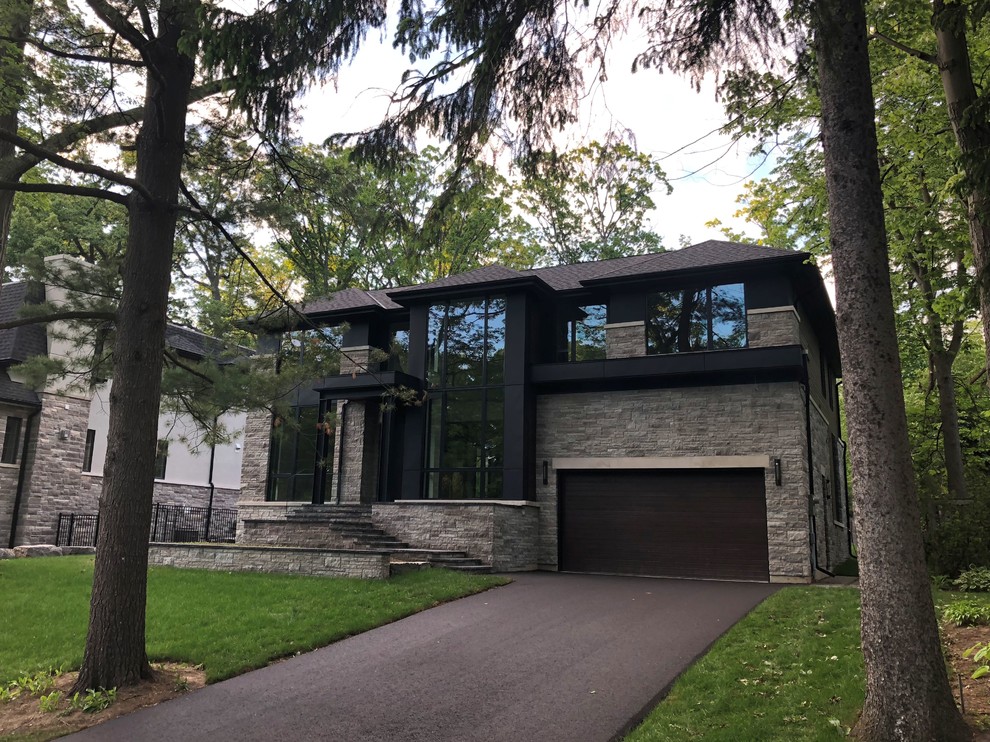 Photo of a large contemporary two-storey black house exterior in Toronto with a hip roof, a shingle roof, stone veneer and a black roof.