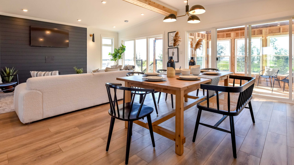 Cette image montre une salle à manger ouverte sur le salon marine de taille moyenne avec un mur blanc, sol en stratifié, un sol marron, un plafond voûté et du lambris de bois.