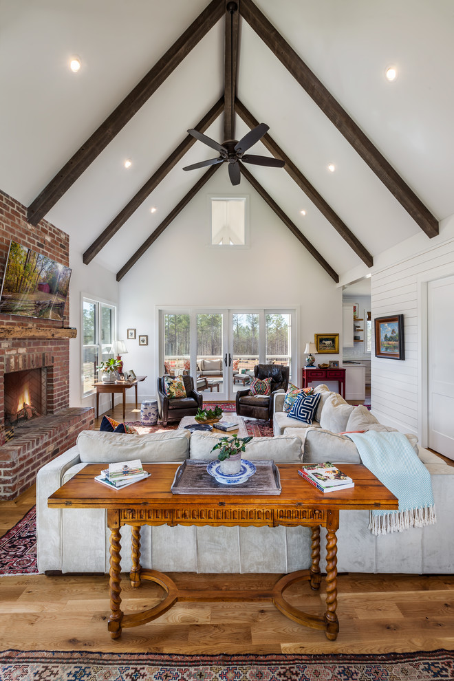 Large country open concept family room in Other with white walls, medium hardwood floors, a brick fireplace surround, a wall-mounted tv, brown floor and a standard fireplace.