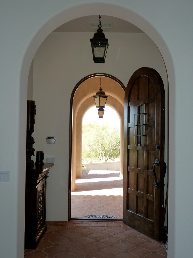 This is an example of a mid-sized mediterranean front door in Phoenix with white walls, terra-cotta floors, a single front door and a dark wood front door.