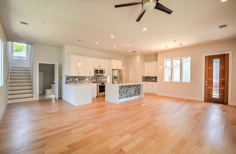 Open concept kitchen - mid-sized transitional single-wall medium tone wood floor and brown floor open concept kitchen idea in Austin with a double-bowl sink, shaker cabinets, white cabinets, marble countertops, gray backsplash, stone tile backsplash, stainless steel appliances, an island and white countertops