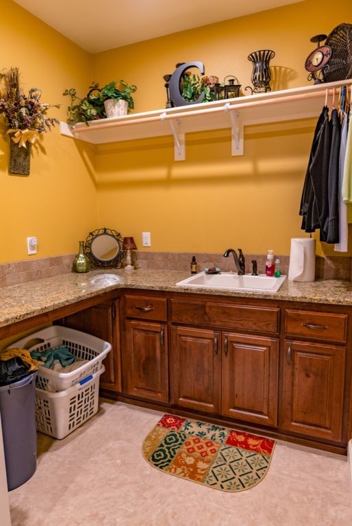 L-shaped dedicated laundry room in Portland with raised-panel cabinets, brown cabinets, granite benchtops, yellow walls, beige floor, multi-coloured benchtop and a drop-in sink.