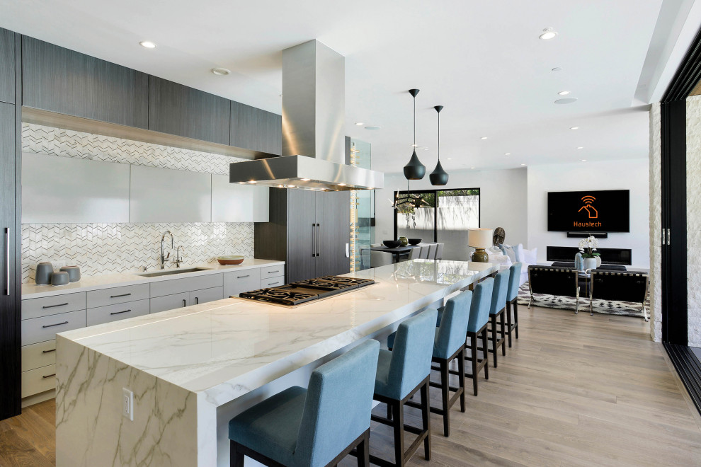 Design ideas for an expansive contemporary galley open plan kitchen in Los Angeles with an undermount sink, flat-panel cabinets, grey cabinets, white splashback, matchstick tile splashback, panelled appliances, light hardwood floors, with island, beige floor and white benchtop.