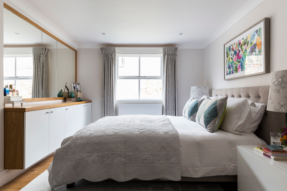 Transitional bedroom in London with grey walls and light hardwood floors.