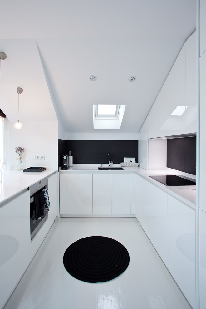 Inspiration for a mid-sized modern u-shaped open plan kitchen in Madrid with an undermount sink, flat-panel cabinets, quartz benchtops, black splashback, ceramic splashback, panelled appliances, painted wood floors, a peninsula and white benchtop.