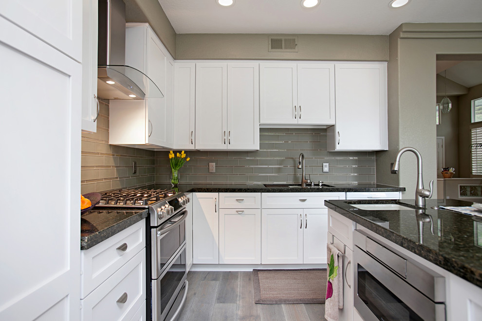 Design ideas for a mid-sized transitional l-shaped eat-in kitchen in San Diego with an undermount sink, recessed-panel cabinets, white cabinets, granite benchtops, grey splashback, glass tile splashback, stainless steel appliances, porcelain floors and with island.