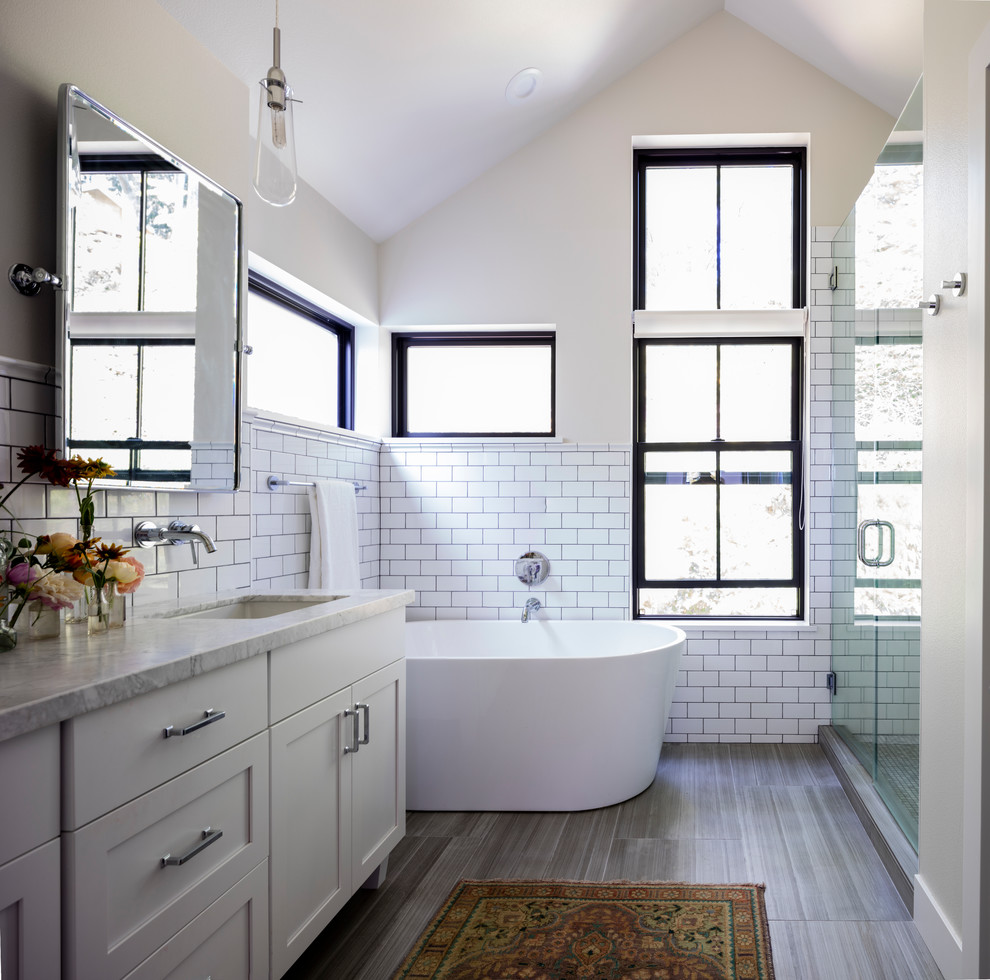 Mid-sized country master bathroom in Seattle with shaker cabinets, white cabinets, a freestanding tub, an alcove shower, white tile, subway tile, beige walls, porcelain floors, an undermount sink, granite benchtops, brown floor, a hinged shower door and grey benchtops.