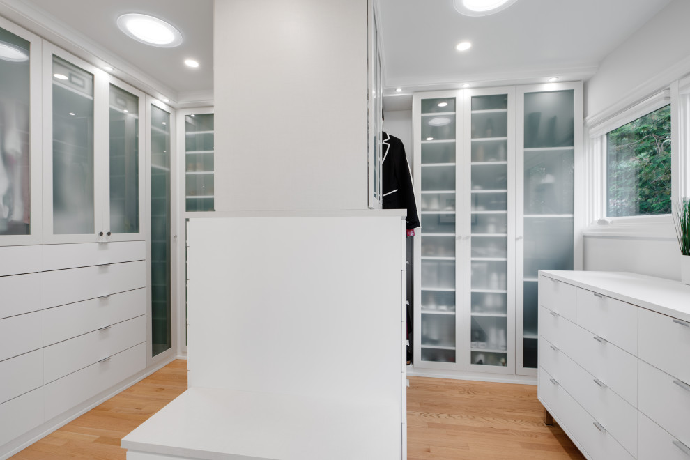 Inspiration for a large retro gender neutral built-in wardrobe in Portland with flat-panel cabinets, white cabinets and light hardwood flooring.