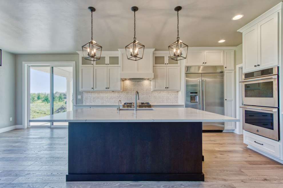Large transitional l-shaped light wood floor and brown floor eat-in kitchen photo with an undermount sink, shaker cabinets, white cabinets, quartz countertops, white backsplash, ceramic backsplash, stainless steel appliances, an island and white countertops