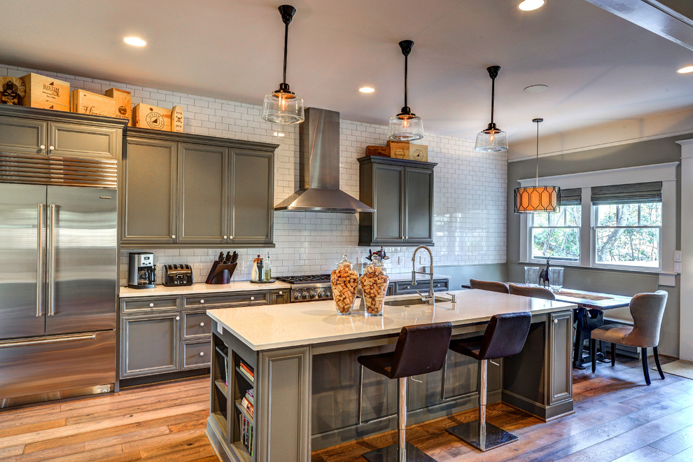 This is an example of a large transitional galley open plan kitchen in Atlanta with an undermount sink, beaded inset cabinets, grey cabinets, quartz benchtops, white splashback, ceramic splashback, stainless steel appliances, medium hardwood floors and with island.