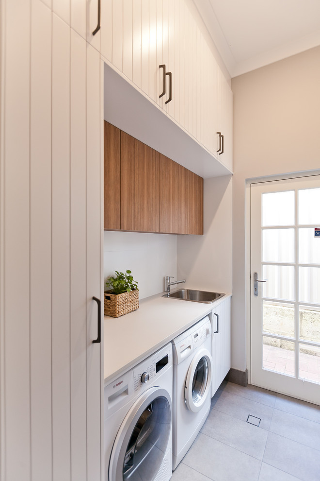 This is an example of a small contemporary galley utility room in Perth with a drop-in sink, light wood cabinets, quartz benchtops, grey walls, porcelain floors, a side-by-side washer and dryer, grey floor and white benchtop.