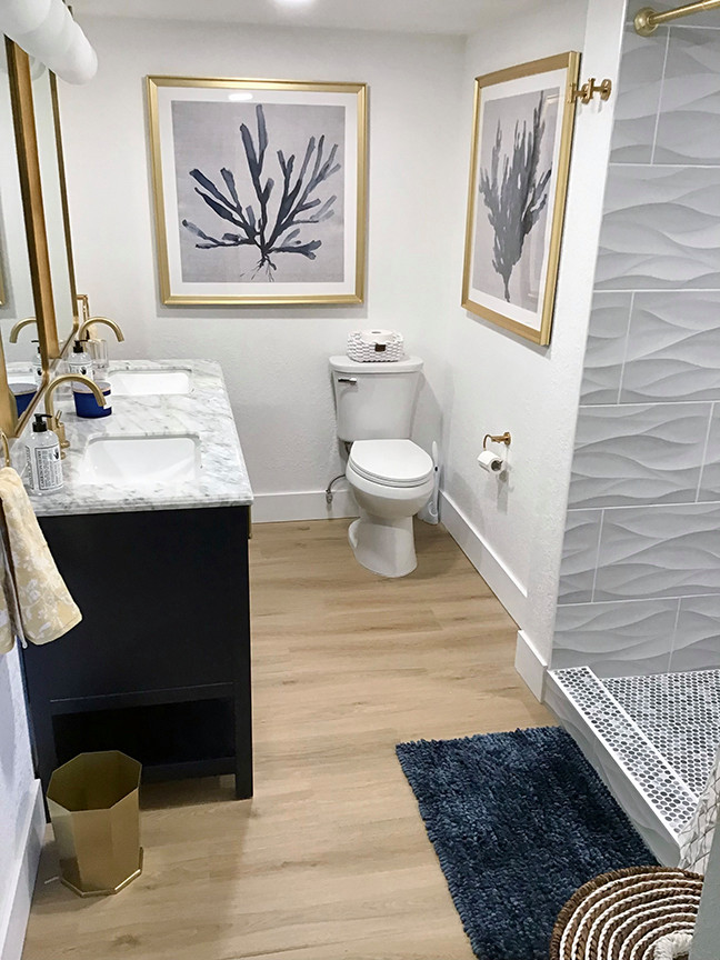 Inspiration for a medium sized nautical ensuite bathroom in Orlando with raised-panel cabinets, blue cabinets, white walls, laminate floors, a submerged sink, engineered stone worktops, brown floors, grey worktops, a freestanding vanity unit, an alcove shower, a two-piece toilet, white tiles, porcelain tiles, a shower curtain and double sinks.