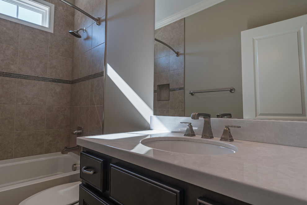 Alcove bathtub - mid-sized transitional kids' beige tile and ceramic tile ceramic tile alcove bathtub idea with shaker cabinets, black cabinets, a two-piece toilet, beige walls, an undermount sink and solid surface countertops