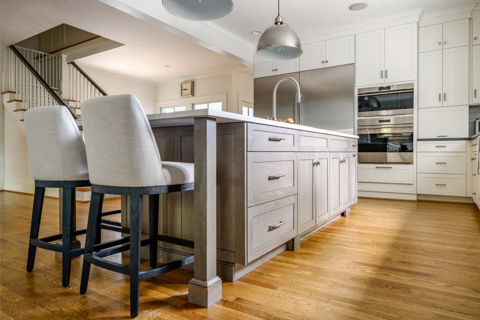 Example of a large transitional galley medium tone wood floor and brown floor eat-in kitchen design with an undermount sink, shaker cabinets, white cabinets, quartz countertops, white backsplash, marble backsplash, stainless steel appliances, an island and white countertops