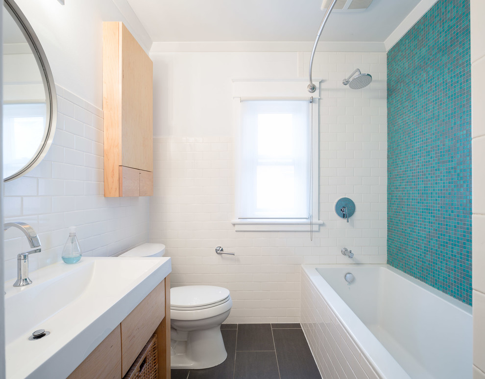 Small contemporary bathroom in Ottawa with an integrated sink, flat-panel cabinets, light wood cabinets, solid surface benchtops, a drop-in tub, a shower/bathtub combo, a one-piece toilet, multi-coloured tile, mosaic tile, white walls and ceramic floors.