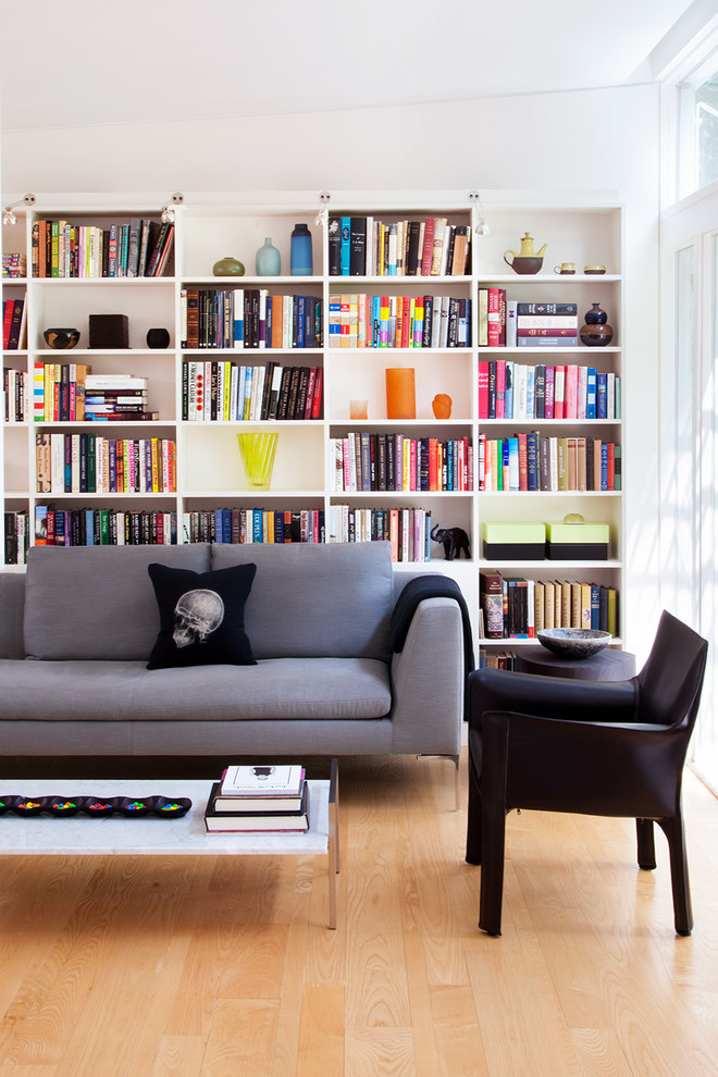 This is an example of a midcentury living room in Philadelphia with a library, white walls and light hardwood floors.