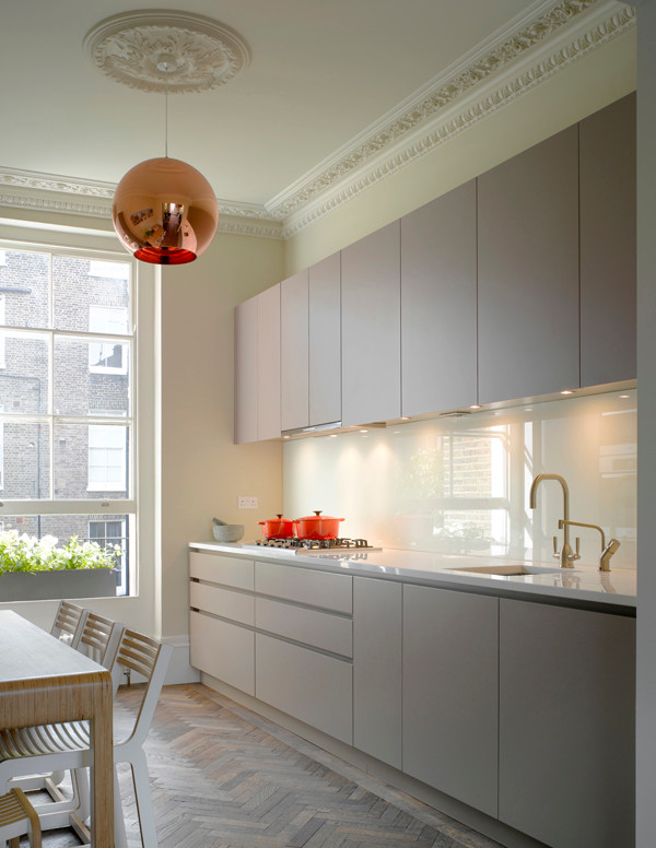 Inspiration for a mid-sized contemporary galley eat-in kitchen in London with flat-panel cabinets, beige cabinets, quartzite benchtops, white splashback, glass sheet splashback, panelled appliances, medium hardwood floors, no island, beige floor and white benchtop.
