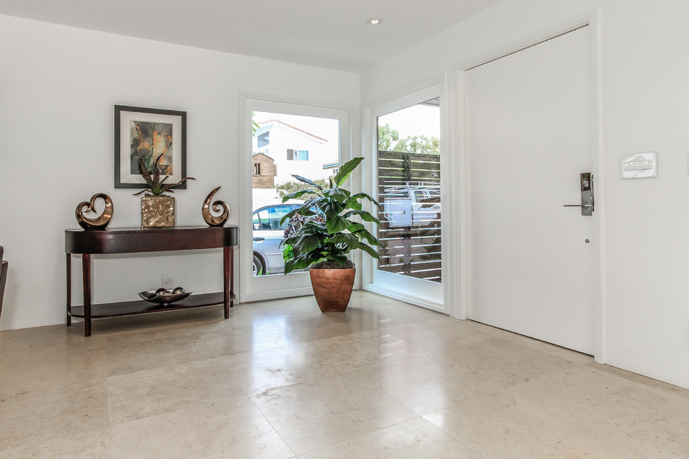 This is an example of a large tropical foyer in Orange County with white walls, limestone floors, a pivot front door and a white front door.