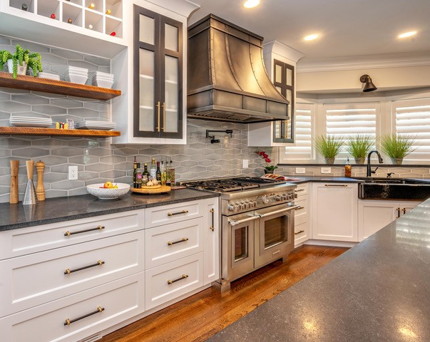 Example of a mid-sized transitional medium tone wood floor and brown floor eat-in kitchen design with a farmhouse sink, shaker cabinets, white cabinets, soapstone countertops, gray backsplash, porcelain backsplash, stainless steel appliances, an island and black countertops
