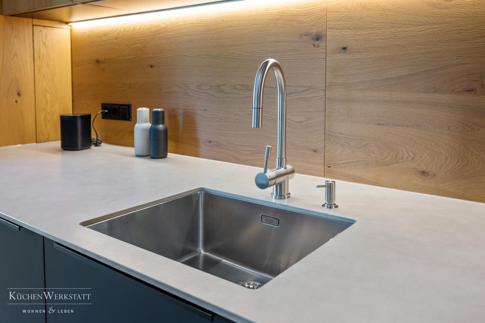 This is an example of a large contemporary galley open plan kitchen in Munich with a submerged sink, flat-panel cabinets, black cabinets, brown splashback, wood splashback, black appliances, concrete flooring, a breakfast bar, grey floors and grey worktops.