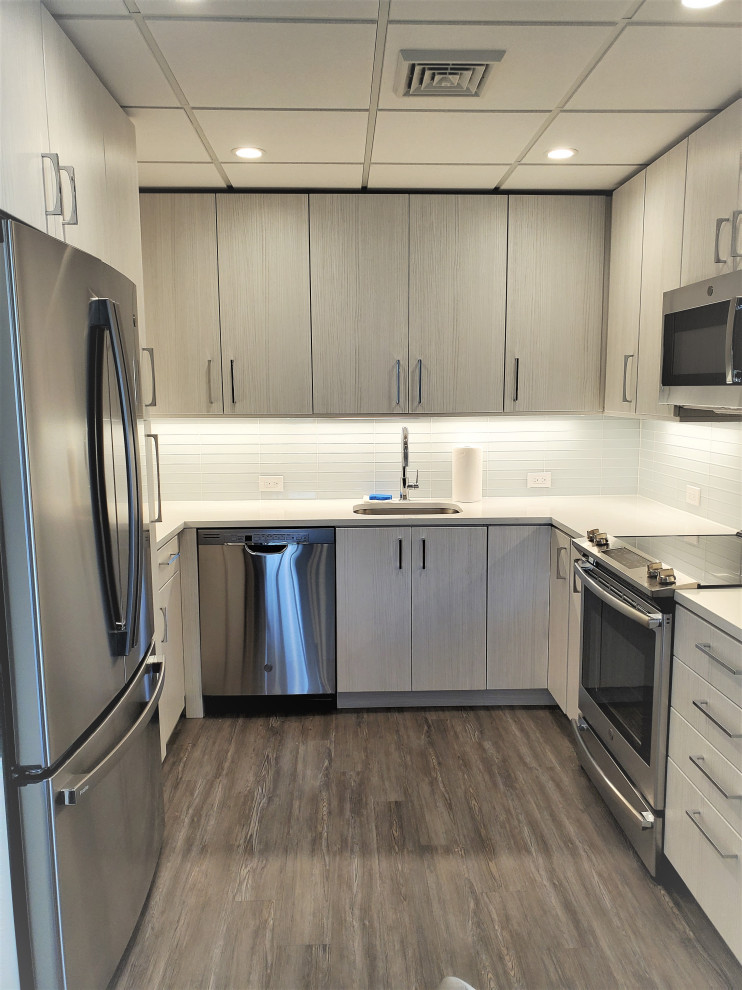 Photo of a small modern u-shaped separate kitchen in Philadelphia with an undermount sink, flat-panel cabinets, grey cabinets, quartz benchtops, white splashback, glass tile splashback, stainless steel appliances, vinyl floors, no island, brown floor and white benchtop.