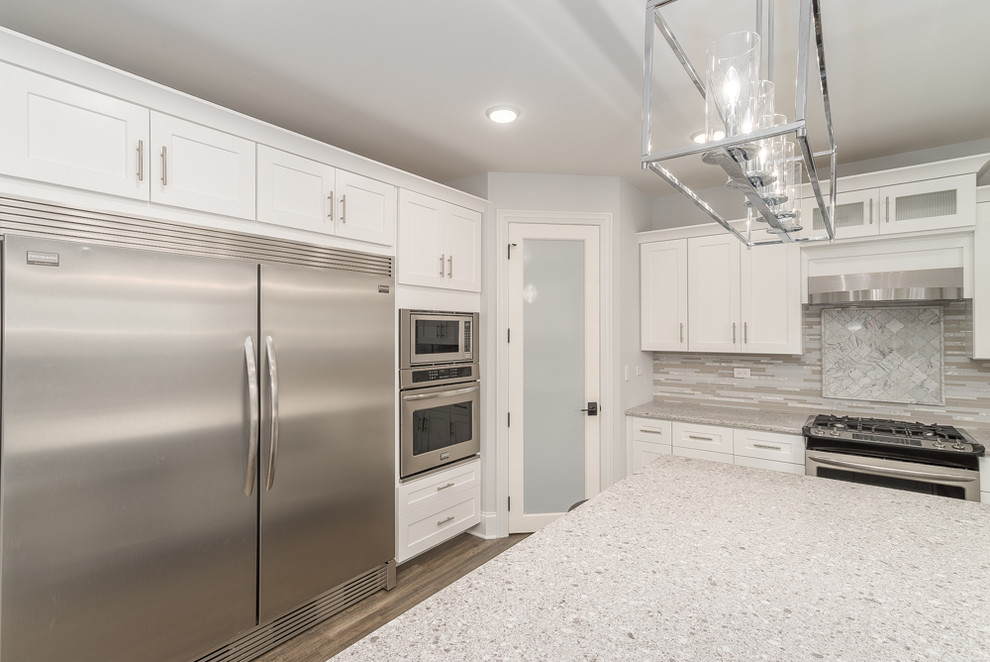 Large transitional u-shaped eat-in kitchen in Chicago with an undermount sink, white cabinets, stainless steel appliances, with island, recessed-panel cabinets, terrazzo benchtops, grey splashback, matchstick tile splashback, light hardwood floors, grey floor and grey benchtop.