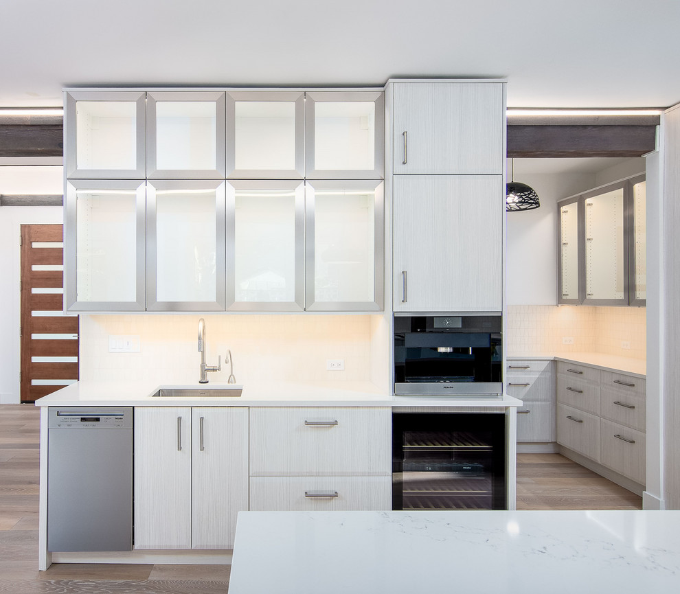 Expansive midcentury galley open plan kitchen in Portland with an undermount sink, flat-panel cabinets, white cabinets, quartz benchtops, white splashback, limestone splashback, stainless steel appliances, light hardwood floors, with island, brown floor and white benchtop.