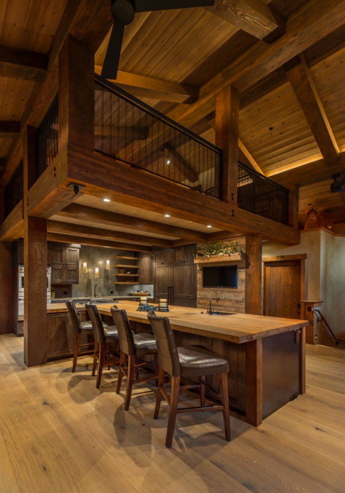 Example of a mountain style l-shaped open concept kitchen design with a farmhouse sink, recessed-panel cabinets, dark wood cabinets, stainless steel appliances and an island