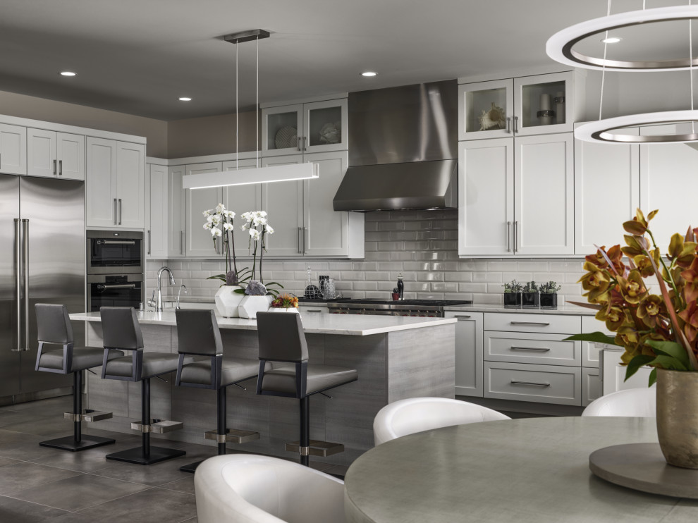 Photo of a contemporary l-shaped kitchen in Denver with shaker cabinets, white cabinets, grey splashback, subway tile splashback, with island, grey floor and white benchtop.