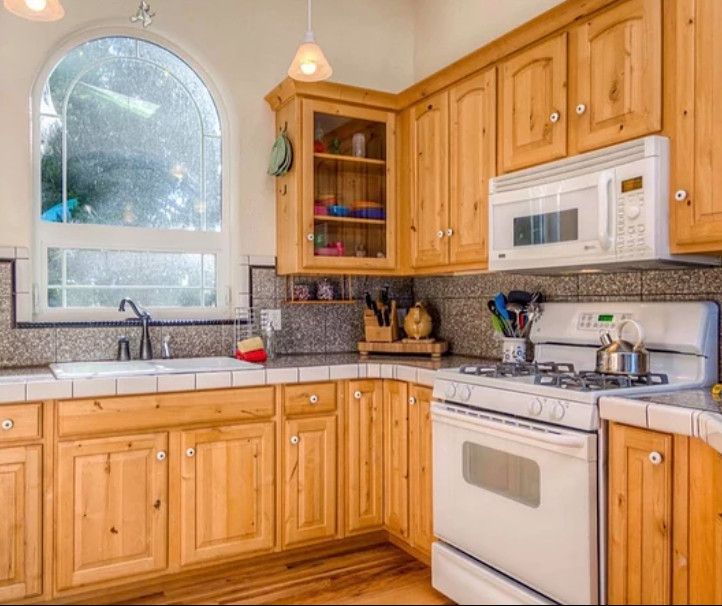 Small mountain style l-shaped light wood floor and beige floor open concept kitchen photo in Seattle with a drop-in sink, raised-panel cabinets, light wood cabinets, gray backsplash, porcelain backsplash, white appliances, no island and gray countertops