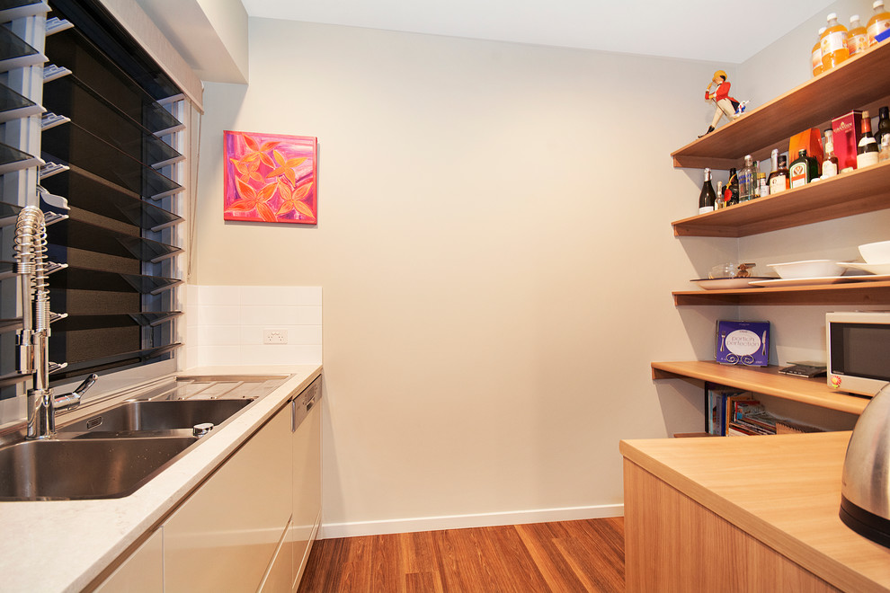 Design ideas for a mid-sized asian kitchen pantry in Sunshine Coast with a double-bowl sink, solid surface benchtops, stainless steel appliances, vinyl floors, beige cabinets, white splashback and ceramic splashback.
